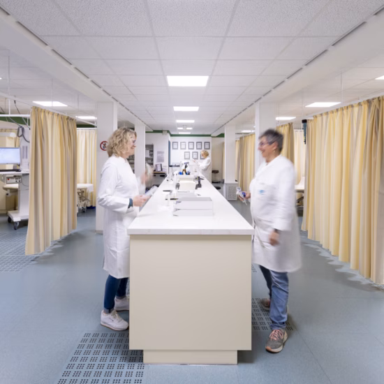 Medical staff in white coats work in a bright, modern clinical classroom equipped with individual treatment rooms, examination tables, and computers.