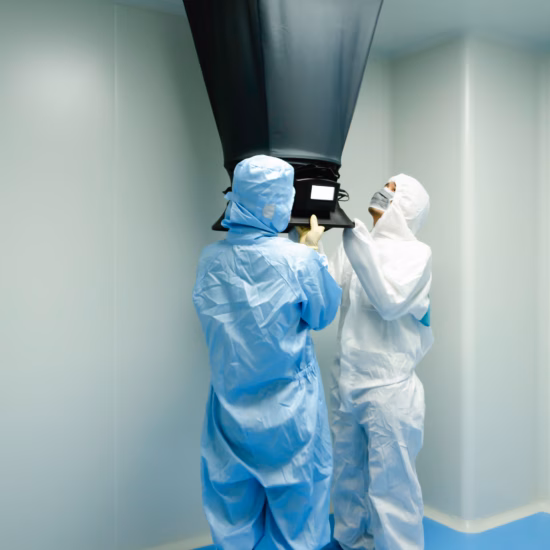Twee medewerkers in cleanroomkleding voeren luchtkwaliteitsmeting uit met een flowhood onder een ventilatieopening
