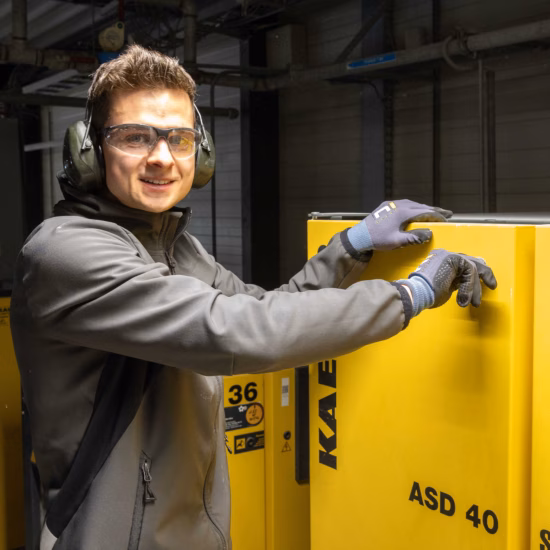 Un employé effectue des travaux sur une installation de compresseurs industriels en portant des équipements de protection individuelle.