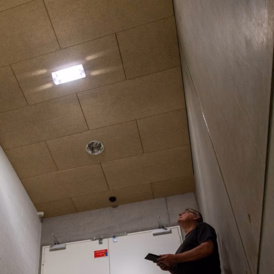 Een persoon kijkt omhoog naar het plafond in een trappenhuis tijdens een visuele controle van de noodverlichting.