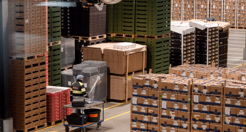Warehouse with stacked pallets, cardboard boxes, and an autonomous mobile robot for internal transport.