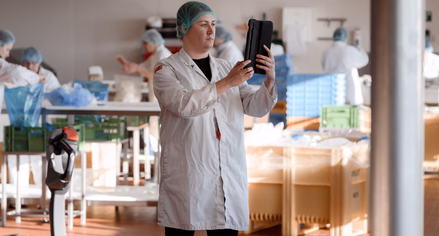 Ein Mitarbeiter in einem weißen Laborkittel inspiziert schwarze Schalen in einer Produktionsumgebung zur Qualitätskontrolle.