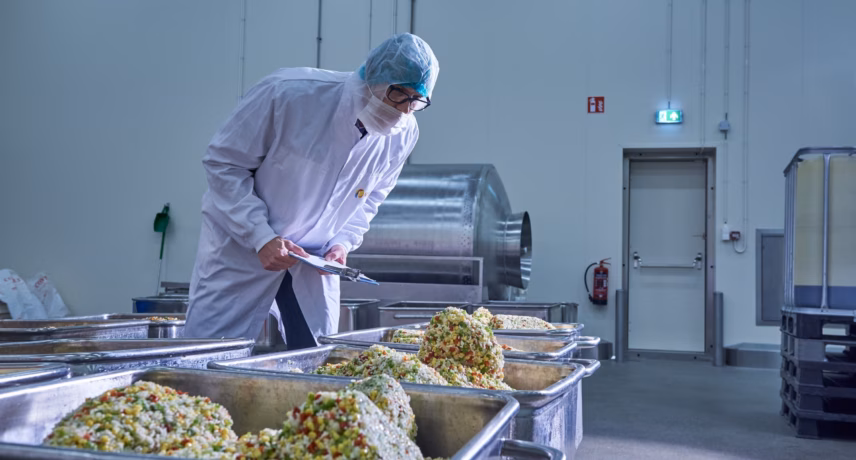 Ein Mitarbeiter in Schutzkleidung verarbeitet Lebensmittel in einem Produktionsraum für die Lebensmittelverarbeitung.