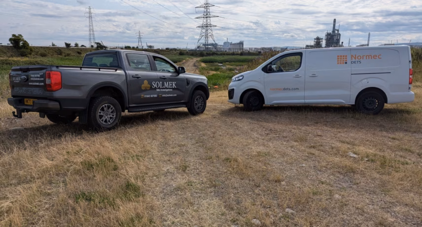 Bedrijfsvoertuigen van Normec DETS en Solmek op een industriële locatie in het veld.