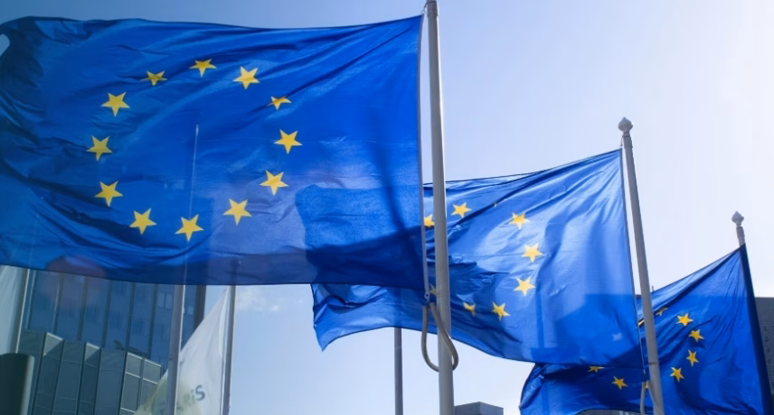 Des drapeaux européens flottent devant un immeuble de bureaux moderne.