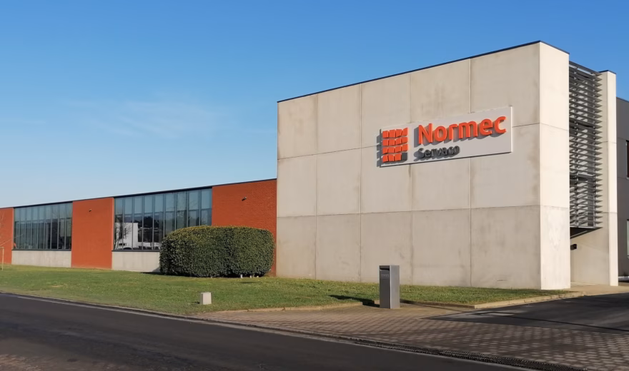 Front view of the modern Normec Servaco building with white and dark grey façades, large windows and the Normec Servaco logo, photographed on a clear sunny day.