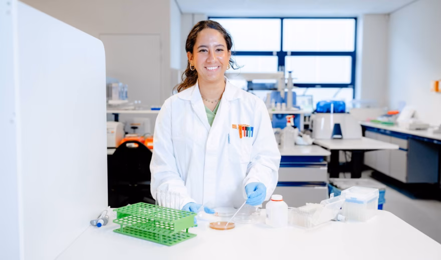 A person in a lab coat is working at a lab table with test tube racks and testing materials in a modern research environment.