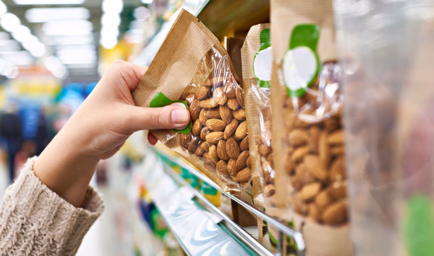 A hand picks up a bag of almonds from the store shelf with packaged nuts.