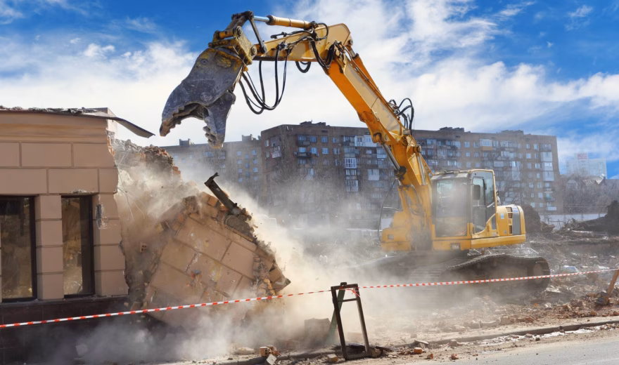 Ein Bagger reißt ein Gebäude während der Abbrucharbeiten auf einer Baustelle ab, auf der viel Staub entsteht.