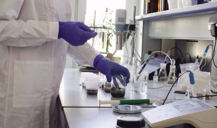 Ein Laborassistent bereitet an einem Laborarbeitstisch mit Mess- und Prüfgeräten eine Probe für die Analyse vor.