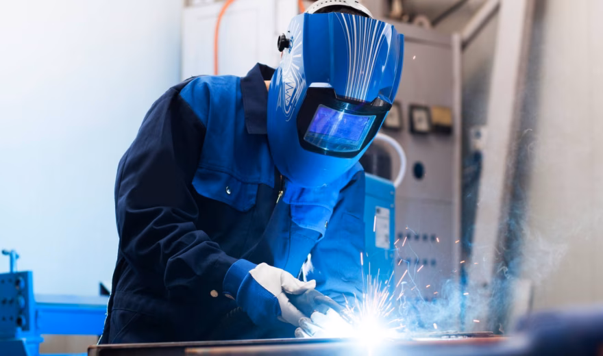 Ein Schweißspezialist führt MIG/MAG-Schweißarbeiten an einer Metallkonstruktion in einer industriellen Werkstatt durch.