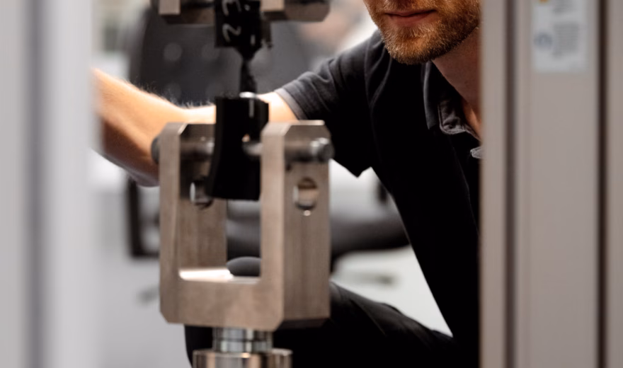 Eine Person überprüft während einer mechanischen Materialprüfung eine Zugversuchsanordnung in einer Universal-Materialprüfmaschine.