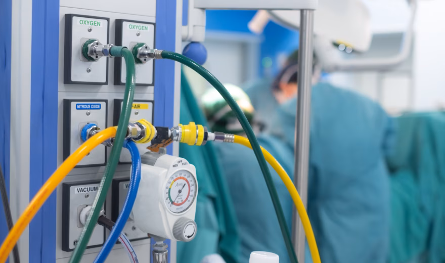 Medisch gassysteem in een operatiekamer met aansluitingen voor zuurstof, lachgas, vacuüm en medische lucht, inclusief gekleurde slangen en drukmeter.