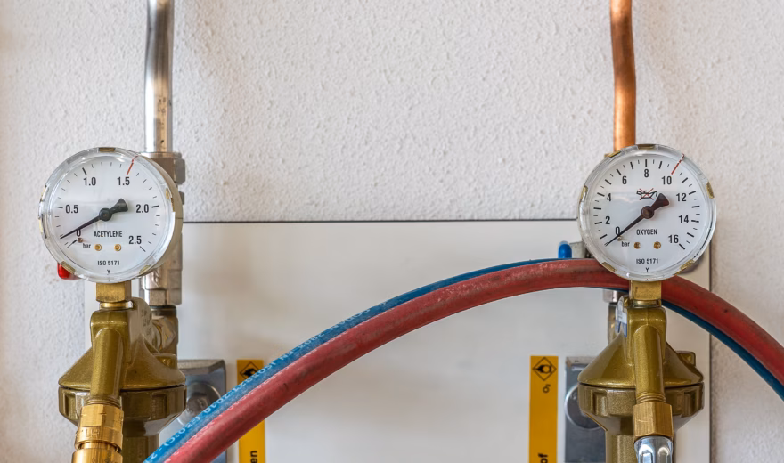 Wandgemonteerde zuurstof‑ en acetyleenregelaars met drukmeters en gekleurde slangen, gebruikt voor professionele zuurstof‑acetyleen lasapparatuur.