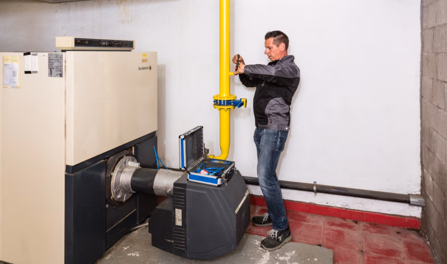 Technicus voert emissiemetingen uit aan een gasinstallatie met gele gasleiding, veiligheidsventiel en meetinstrument voor rookgas- en CO‑analyse.