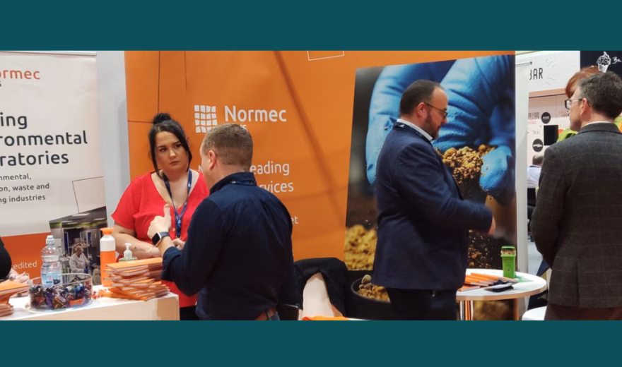 Normec-stand tijdens een evenement, waar bezoekers met elkaar in gesprek zijn bij de beursopstelling van milieulaboratoria.