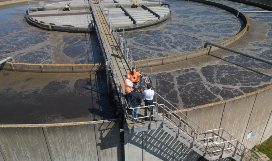Medewerkers inspecteren een waterzuiveringsinstallatie met ronde nabezinktanks.