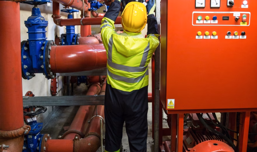 Een medewerker controleert een technische installatie met leidingwerk en besturingsapparatuur in een industriële omgeving.