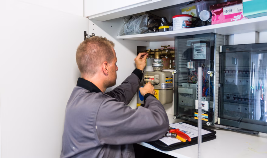 Un technicien effectue des opérations de contrôle sur un compteur de gaz et l'installation électrique d'un placard à compteurs.