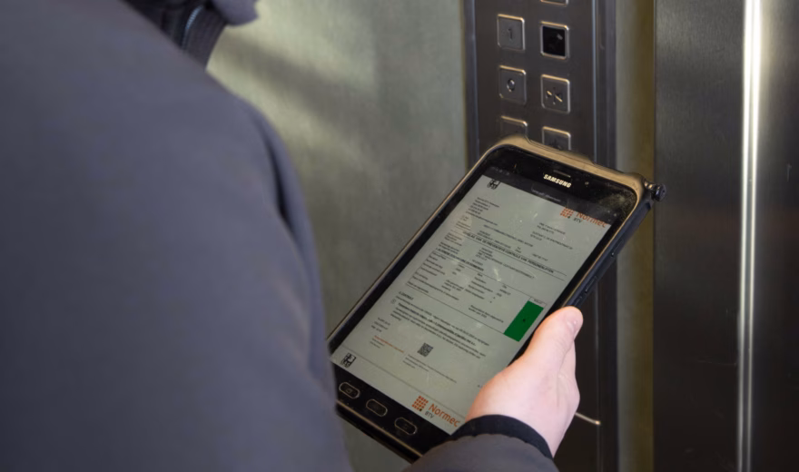 Un inspecteur contrôle une installation d'ascenseur et consigne ses constatations sous forme numérique pendant l'inspection.