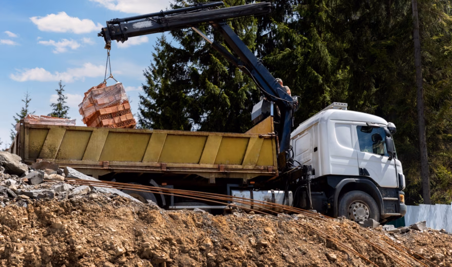 Een vrachtwagen met kraan verplaatst bouwmaterialen op een bouwplaats.