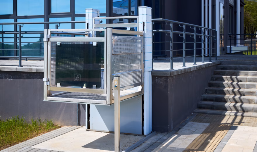 Une plate-forme élévatrice offre un accès facilité à côté d'un escalier, à l'entrée d'un bâtiment moderne.