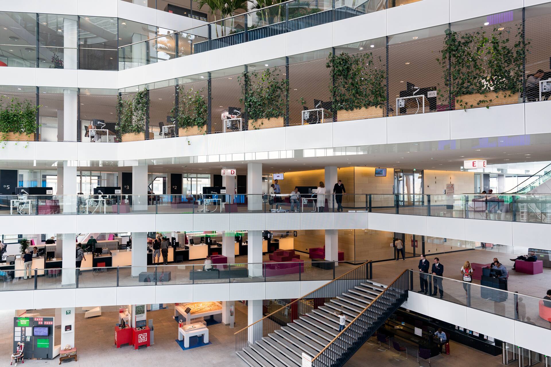 Intérieur d'un immeuble de bureaux moderne avec des espaces de travail ouverts, plusieurs étages et des espaces verts intégrés.