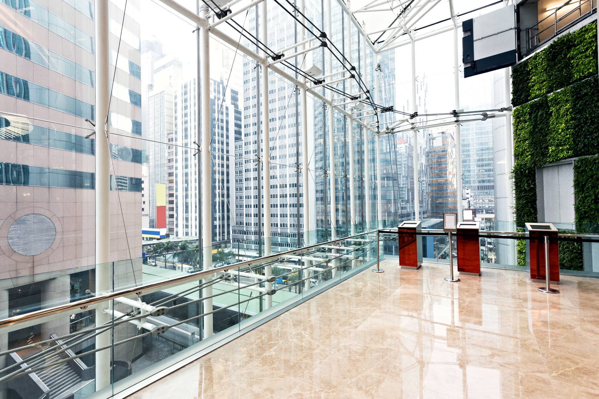 Intérieur d'un immeuble de bureaux moderne avec des structures en verre, une vue sur des gratte-ciel et un mur végétal.