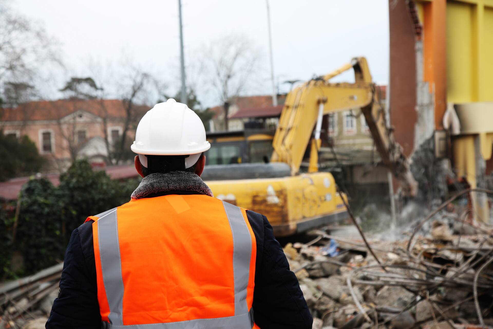 Un superviseur observe les travaux de démolition effectués à l'aide d'une pelleteuse sur un chantier.