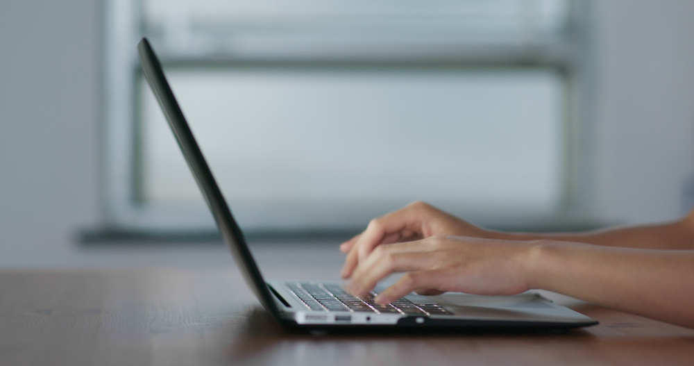 Hands typing on a laptop at a desk in a modern work environment